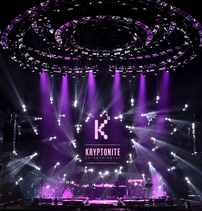 Concert stage with purple beam lights and the Kryptonite Entertainment logo on the screen