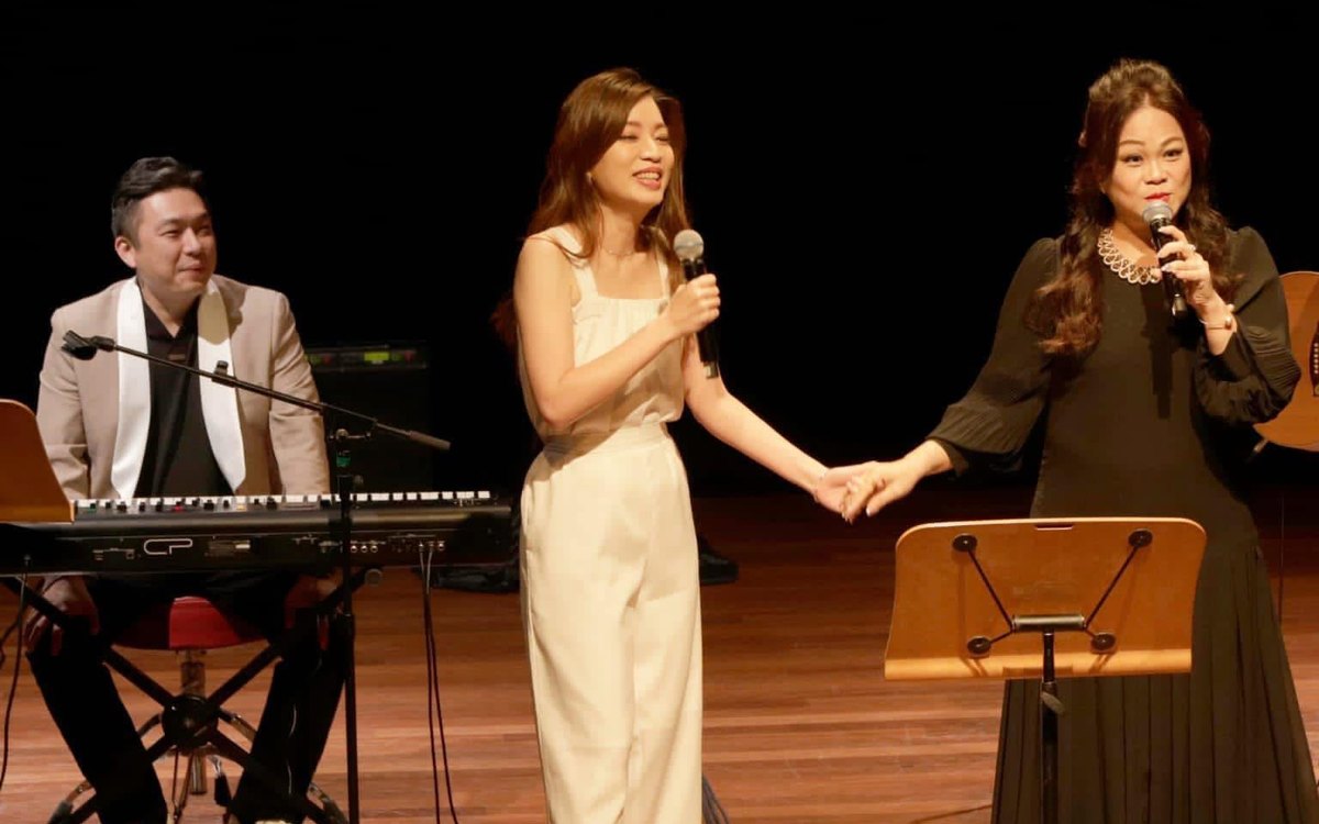 Keyboard player and two female vocalists holding hands on a concert stage